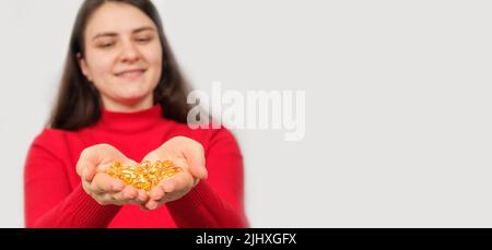 Eine lächelnde Frau hält in ihren Handflächen eine Handvoll Kapseln Fischöl, Omega 3. Banner mit Platz für Text. Stockfoto