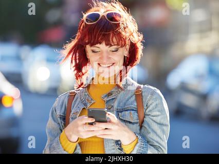 Pläne machen, während shes in der großen Stadt. Eine attraktive junge Frau, die ihre Nachrichten überprüft, während sie in der Stadt unterwegs ist. Stockfoto