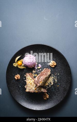 Blätterkuchen mit Schokoladenpudding, Walnuss- und Heidelbeer-Eis auf schwarzem Teller Stockfoto