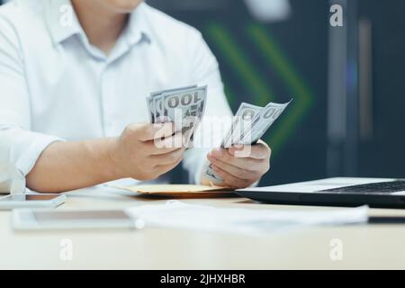 Nahaufnahme der Hände eines Geschäftsmannes in einem Hemd, der Geld in Dollar zählt, arbeitet ein Geschäftsmann in einem modernen Büro Stockfoto