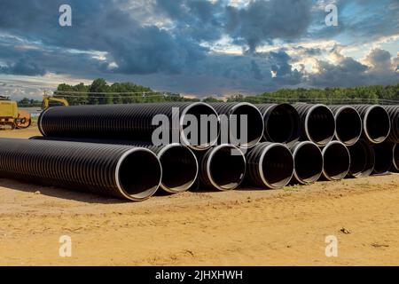 Auf einer Baustelle befinden sich Reihen neuer schwarzer PVC-Kunststoffrohre, die in Reihen für Abflusssysteme gestapelt sind. Stockfoto