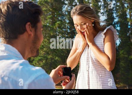 Für immer bei euch zu sein, wäre eine Ehre. Ein junger Mann schlägt seiner Freundin in der Natur vor. Stockfoto