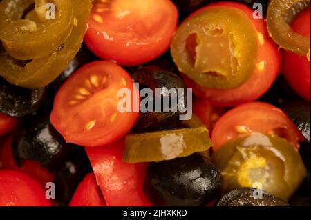 Gemüsesalat aus Tomaten, schwarzen Oliven und eingelegtem Jalapeno-Pfeffer, gewürzt mit Olivenöl. Gesunde Ernährung, Fitness-Diät. Nahaufnahme der Oberfläche te Stockfoto