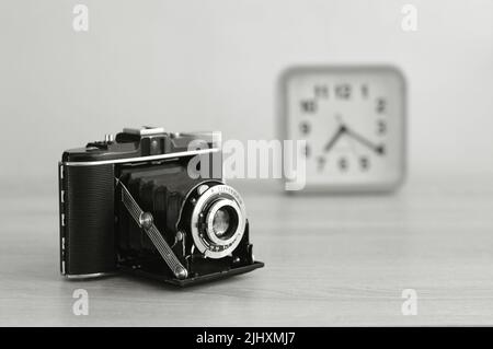 Klassische analoge Mittelformat-Filmkamera und eine Uhr in Schwarz-Weiß. Alte Filmkamera mit Faltenbalg. Stockfoto