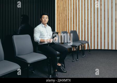 Ein asiatischer Mitarbeiter wartet in der Lobby, ein Mann bekommt einen Job in einem modernen Büro Stockfoto