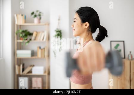 Junge Erwachsene asiatische Frau macht Übungen mit Hanteln im Wohnzimmer Stockfoto