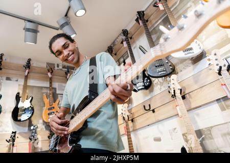 KIEW, UKRAINE - 16. FEBRUAR 2022: Low-Angle-Ansicht des fröhlichen afroamerikanischen Käufers, der im Musikgeschäft E-Gitarre spielt Stockfoto