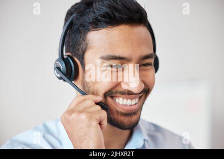 Nahaufnahme eines lächelnden Callcenters mit gemischter Rasse, der lächelt, während er ein Headset trägt. Junger männlicher Kundendienstmitarbeiter mit schnurlosem Headset und Stockfoto