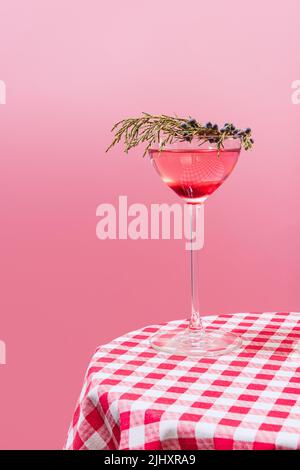 Ein Glas köstlicher alkoholischer Getränke mit Beeren, ein kosmopolitischer Cocktail auf karierten Tischdecken, isoliert im pfirsichfarbenen Hintergrund. Stockfoto