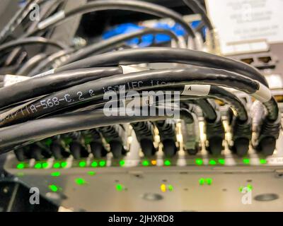 Ethernet-Kabel, die mit Netzwerkgeräten verbunden sind und im Rechenzentrum grün leuchten Stockfoto