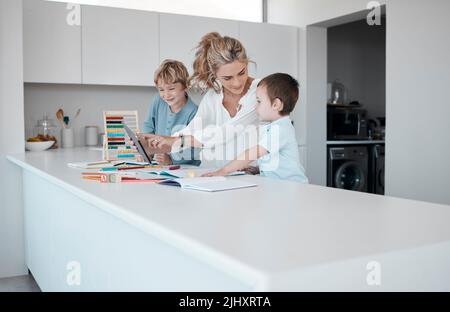 Alleinerziehende Mutter, die kleine Söhne während des Homeschool-Unterrichts zu Hause unterrichtet. Autistische niedliche kleine kaukasische Jungen lernen während ihrer Zeit lesen und schreiben Stockfoto