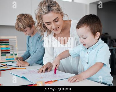 Alleinerziehende Mutter, die kleine Söhne während des Homeschool-Unterrichts zu Hause unterrichtet. Autistische niedliche kleine kaukasische Jungen lernen während ihrer Zeit lesen und schreiben Stockfoto