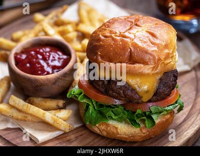 Cheeseburger mit Salat und Tomaten auf geröstetem Brötchen mit pommes Frites und Ketchup auf Holzplatte Stockfoto