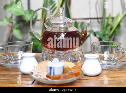 Earl Grey Tee in Glas Teekannen mit Tassen und kristallisierten Früchten auf Holz Hintergrund Stockfoto