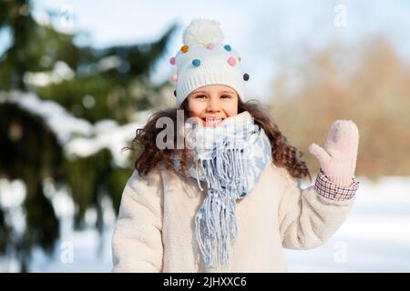 Glückliches kleines Mädchen winkt im Winter mit der Hand im Freien Stockfoto