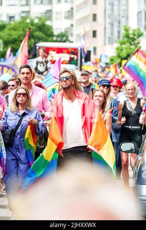 Ein junger, gutaussehender Mann, der die Straße entlang läuft, mit einer Gruppe anderer Menschen, die eine stolze Fahne auf seinen Schultern tragen, drapierte bei Malmo Pride Sweden Stockfoto