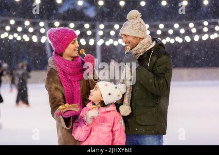 Glückliche Familie, die Pfannkuchen auf der Eislaufbahn isst Stockfoto