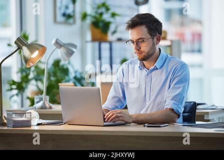 Ein Meister bei der Arbeit. Ein junger Geschäftsmann, der an seinem Schreibtisch an seinem Laptop arbeitet. Stockfoto