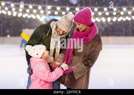 Glückliche Familie, die Pfannkuchen auf der Eislaufbahn isst Stockfoto