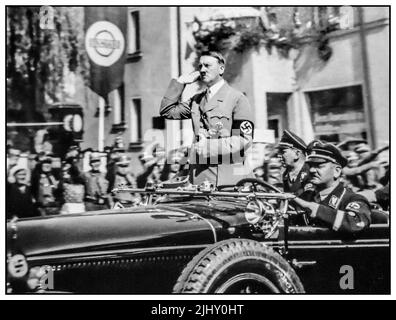 Adolf Hitler steht in seinem offenen Mercedes-Motorwagen, grüßt seine Truppen und begrüßt Menschenmengen, indem Heil Hitler Nazi-Deutschland 1930s begrüßt Stockfoto