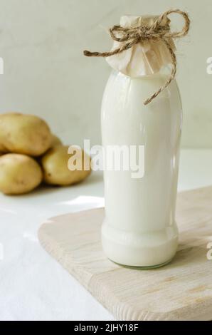 Glasflasche mit Kartoffelmilch auf dem Tisch. Ein neuer Trend in der gesunden Ernährung. Konzept für alternative Lebensmittel. Pflanzliche Milch für Veganer. Vertikale Ausrichtung. Stockfoto