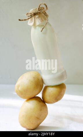 Glasflasche mit Kartoffelmilch auf dem Tisch. Ein neuer Trend in der gesunden Ernährung. Konzept für die Levitation von Lebensmitteln. Pflanzliche Milch für Veganer. Vertikale Ausrichtung. Stockfoto