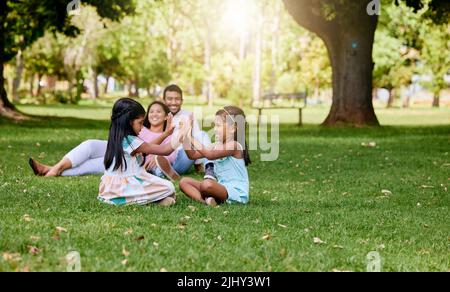Ein glückliches asiatisches Paar, das draußen auf Gras liegt, genießen liebende Eltern die Zeit mit ihren kleinen Töchtern, die ein Spiel spielen. Verbinden Stockfoto