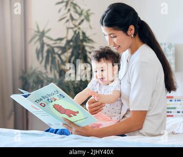 Mutter liest ihrem Baby vor. Elternteil liest ein Storybook. Glückliche Frau, die ihrem Kind vorliest. Mutter hält aufgeregt Baby. Kleines Mädchen, das von einer Geschichte begeistert ist Stockfoto