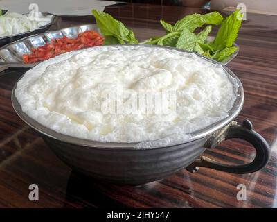 Buttermilch, traditionelles Joghurtgetränk oder Getränk, das in der Türkei als Ayran bekannt ist, mit Schaum in silbernem Metallbecher auf dem Tisch. Buttermilch, traditionell Stockfoto