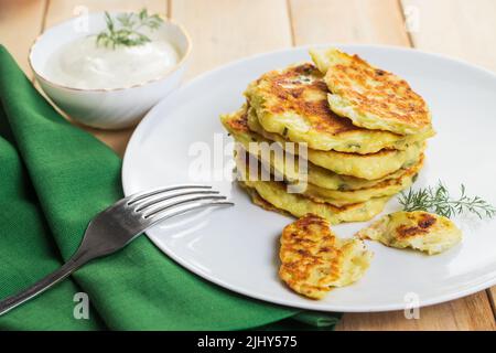 Stapel Zucchini fritters in Teller und Sahnesauce. Gericht auf grüner Serviette. Gesunde vegane Ernährung Lebensmittel auf Holz Hintergrund. Stockfoto
