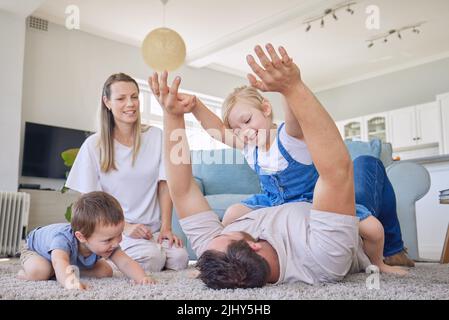 Familie mit Tochter und Baby-Sohn, die im Wohnzimmer auf dem Teppich spielten. Papa spielt mit seinem kleinen Mädchen und Baby, während die Mutter dazusitzt und sie beobachtet Stockfoto