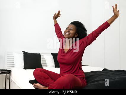 Am frühen Morgen wird eine wunderschöne afrikanische Frau die Arme nach außen strecken, während sie auf dem Bett sitzt und Platz für Kopien hat Stockfoto