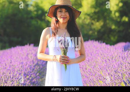 Schöne Frau in weißem Kleid mit einem Strauß Lavendel auf der Hand. Stockfoto