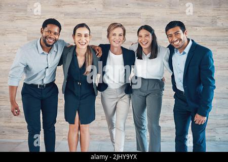 Wir erreichen mehr als ein Team. Eine vielfältige Gruppe von Geschäftsleuten, die im Büro mit den Armen um sich stehen. Stockfoto