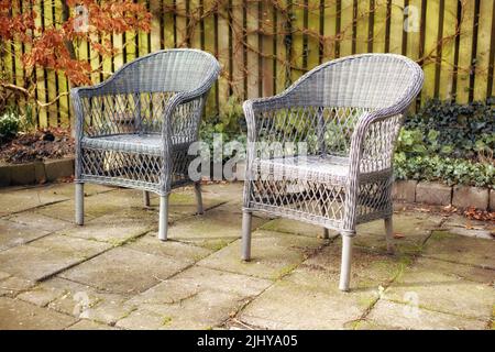 Sessel in einem entspannenden Gartenbereich in einem Hinterhof eines Hauses. Dekorative Gartenmöbel oder gewebte Stühle in der Nähe von Zierpflanzen. Garteneinrichtung Stockfoto