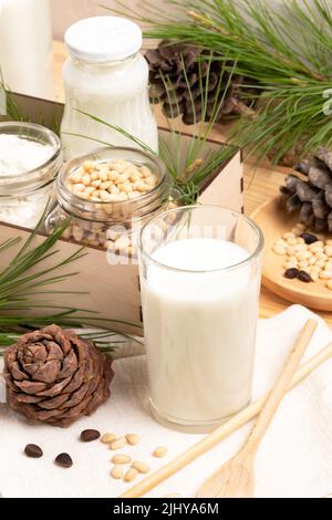 Zedernmilch in Glas und Flasche, Zutaten Nüsse und Mehl in Gläsern in Box, Kegel, Zweige, Löffel. Alternative Milch ohne Milchprodukte. Gesunde Bio-Milch re Stockfoto