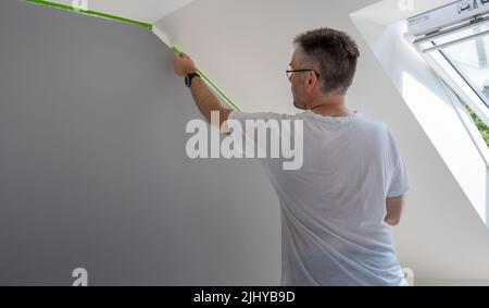 Painter entfernt Klebeband und erstellt einen scharfen Rand zwischen einem grau-weiß lackierten Teil einer Wand. Stockfoto