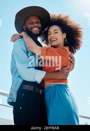 Porträt von zwei jungen, vielfältigen Menschen, die sich umarmen und lächeln, während sie draußen modische Kleidung tragen. Gemischtes afroamerikanisches Paar Stockfoto