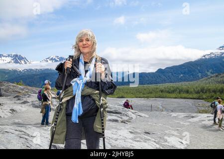 2022 06 24 Exit Glacier Alaska USA Senior Lady beim Wandern auf unwegsamem Gelände mit Wanderstöcken - Mantel um die Taille gebunden - unsere Touristen und nebligen Berge Stockfoto