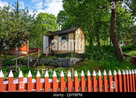 Kleines Holzgartenhaus hinter einem roten Gartenzaun in Schweden Stockfoto