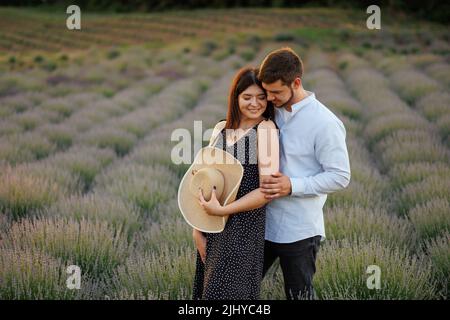 Schönes Paar von Mann und Frau umarmt, während sie in der Mitte des Lavendelfeldes stehen Stockfoto