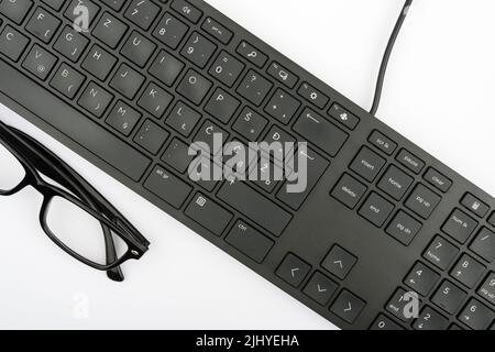 Ein Teil einer schwarzen Computertastatur und eine Brille auf weißem Hintergrund Stockfoto