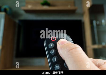 Die Fernbedienung des Fernsehers wechselt den Daumen des Kanals auf dem schwarzen Fernsehbildschirm Stockfoto