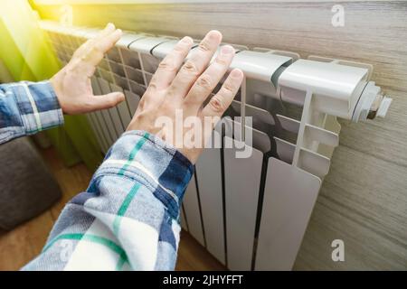 Nahaufnahme eines Mannes Hände, die sie über einer weißen Batterie erwärmt. Draufsicht. Konzept der Probleme mit der Heizung im Winter. Die Energiekrise. Stockfoto