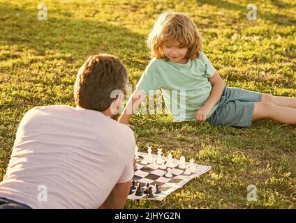 Vater und Sohn spielen Schach auf Gras. Vatertag. Glückliche Familie. Stockfoto