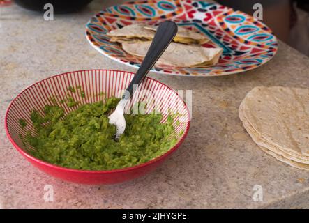 Avocado in einer Schüssel. Gabel in der Schüssel. Mexikanisches Essen im Hintergrund. Stockfoto