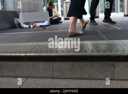 London, England, Großbritannien. Menschen, die an einem Obdachlosen vorbeigehen, der auf den Stufen der Victoria U-Bahnstation bettelt Stockfoto