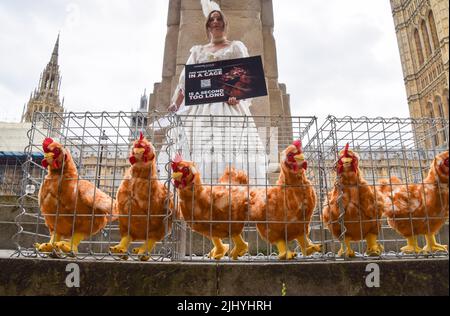 London, England, Großbritannien. 21.. Juli 2022. Ein Protestler steht neben Käfigen mit Plüschhühnern-Spielzeug. Aktivisten der Humane League UK versammelten sich vor dem Parlament, um die Regierung aufzufordern, engen, grausamen Käfigen ein Ende zu setzen, in denen eierlegende Hühner häufig gehalten werden. Der Protest markiert 200 Jahre seit dem ersten Tierschutzgesetz Großbritanniens, bei dem mehrere Aktivisten historische Kleidung trugen. (Bild: © Vuk Valcic/ZUMA Press Wire) Stockfoto