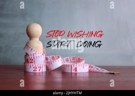 Zitate zu Fitness und Motivation. Holzpuppe und Maßband mit dem Text „STOP WISHING START DOING“ Stockfoto