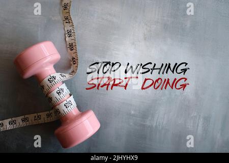 Zitate zu Fitness und Motivation. Kurzhantel und Maßband mit dem Text „STOP WISHING START DOING“ Stockfoto